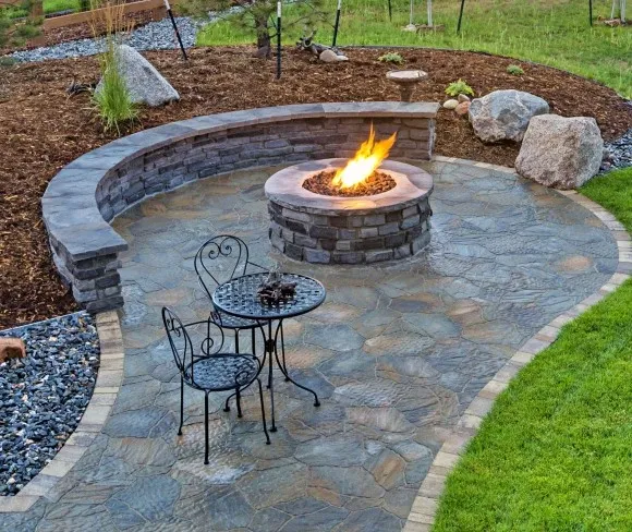 Outdoor stone fire pit surrounded by a circular seating wall and a small table.