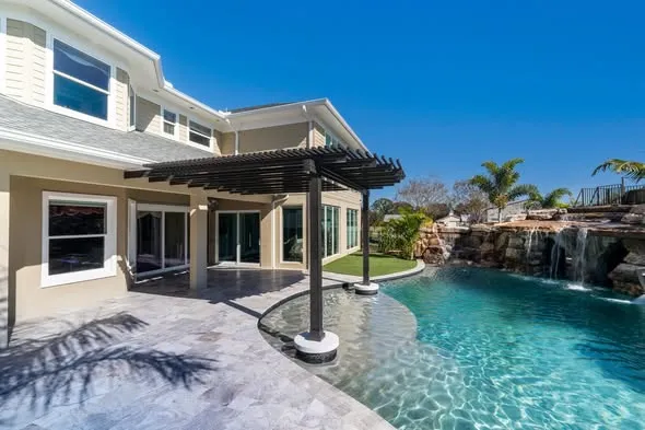 Luxury home with pool, waterfall, and patio under a pergola.